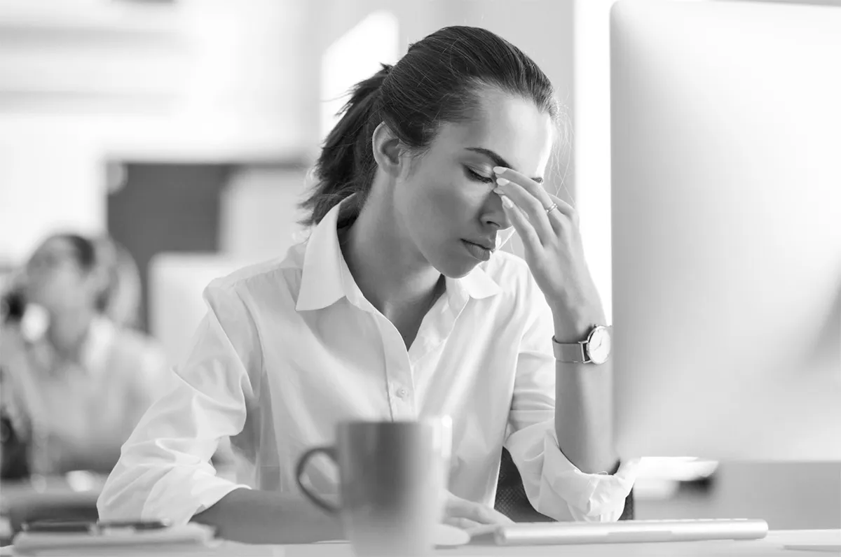 Bild A Eine weibliche Person in schwarz/weiß mit geschlossenen Augen und Hand vor der Stirn
